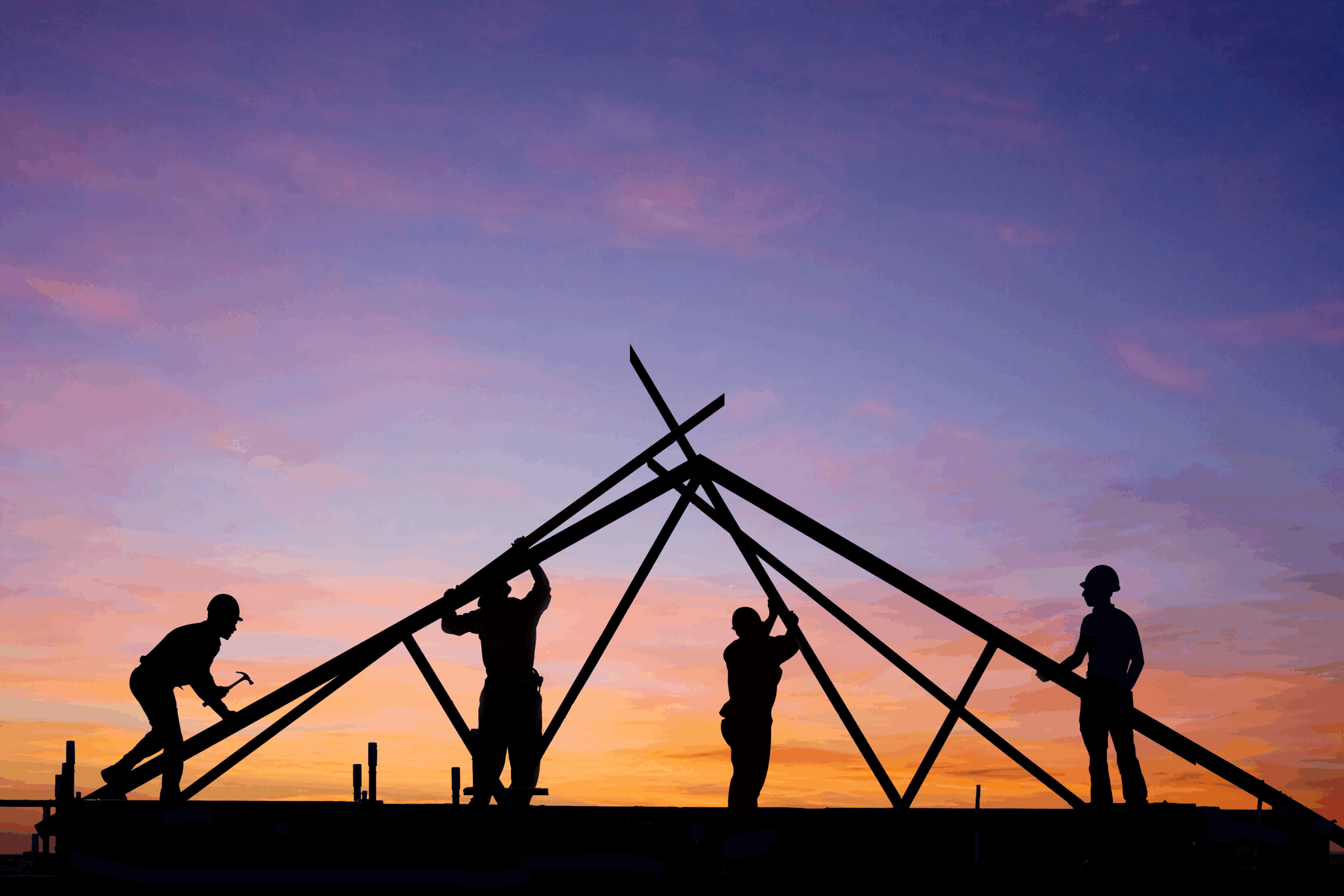 Silhouettes of Four Construction Workers Assembling a Metal Roof Structure at Sunset