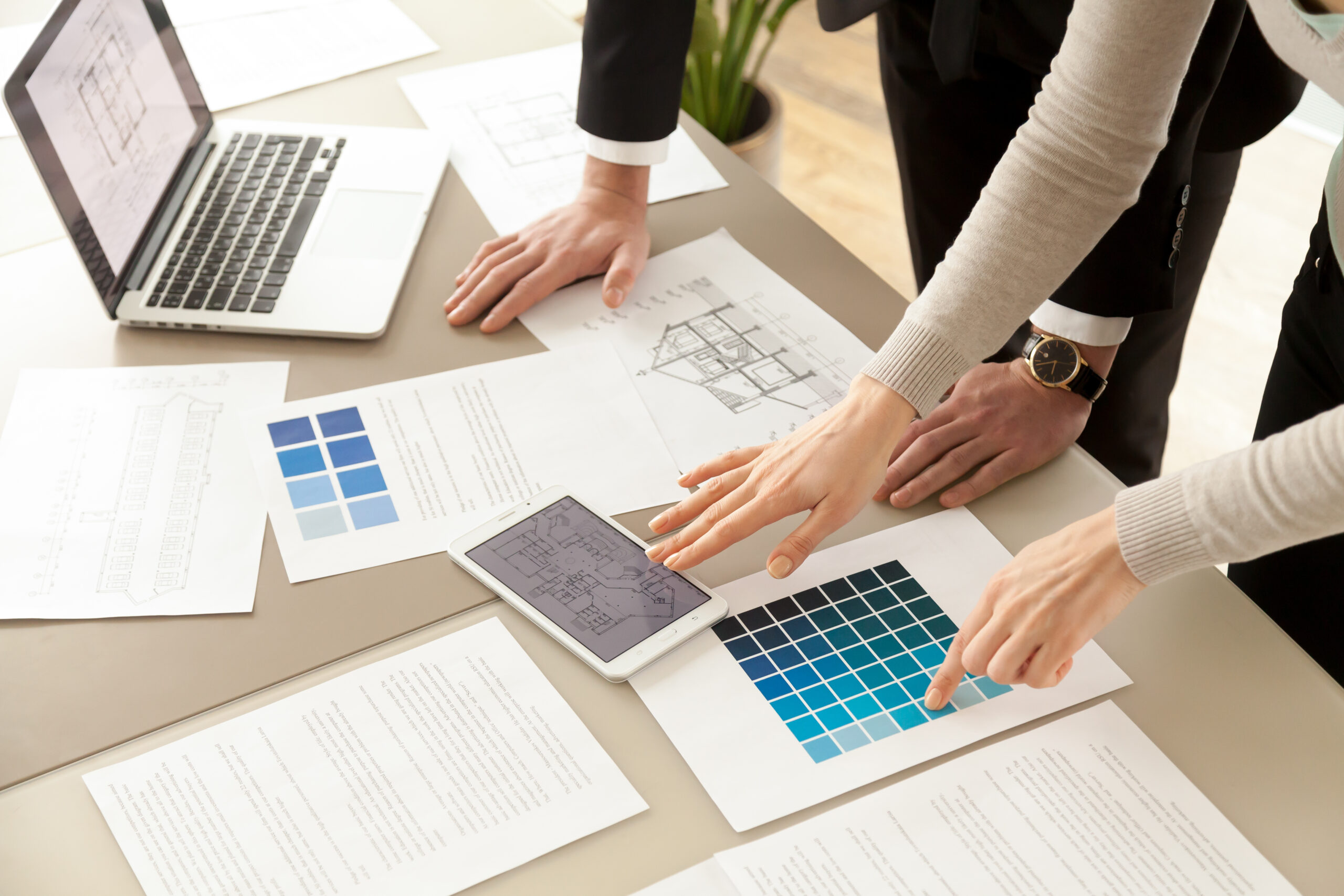 Close Up View of Interior Designers Teamwork with Pantone Swatch and House Building Plans on Office Desk