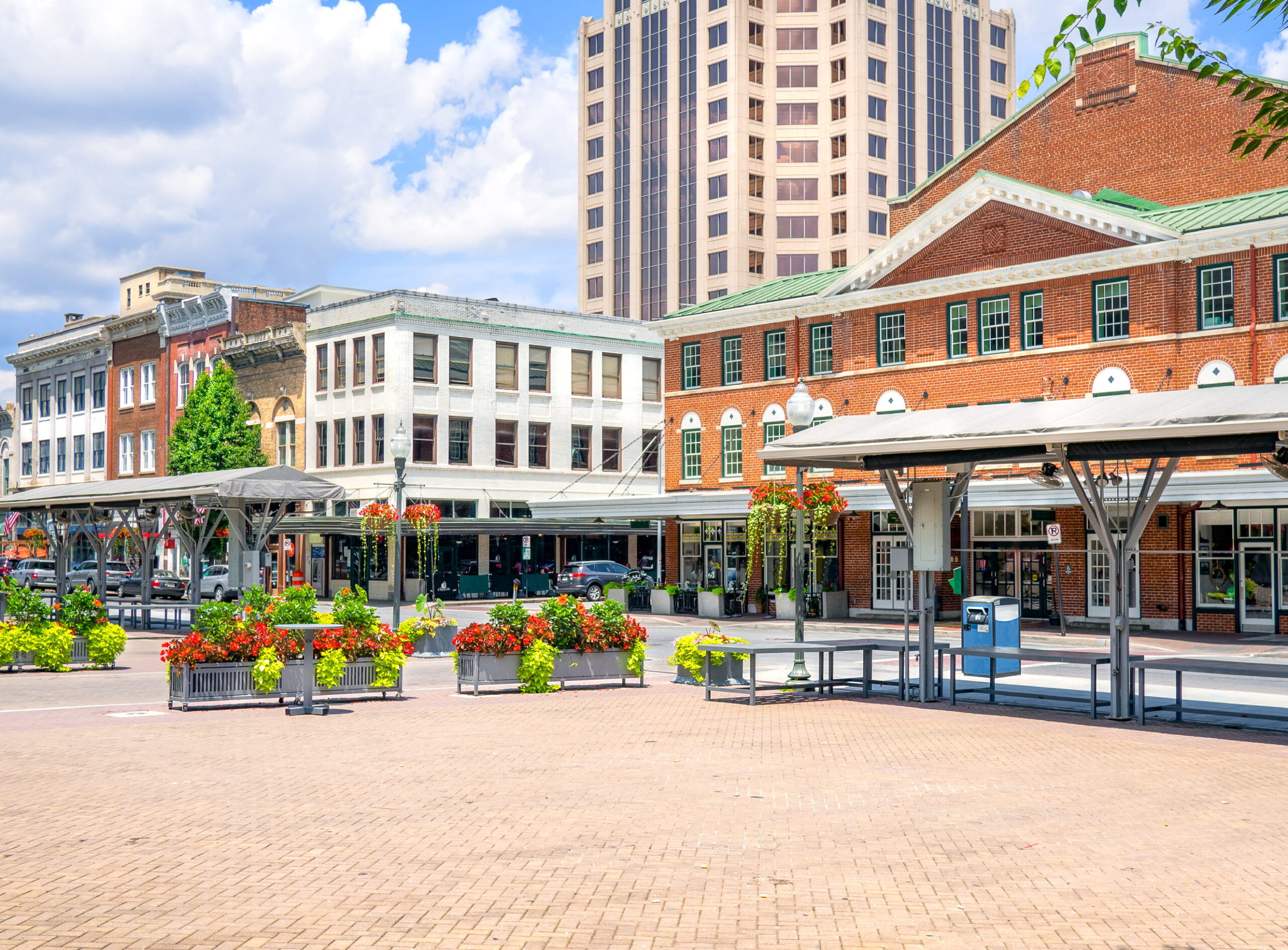 A vibrant town square with historic brick buildings, colorful flowers, and modern skyscrapers. The scene conveys a lively, inviting atmosphere.